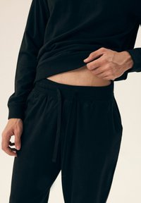 Czarny sweatshirt z prążkowanym wykończeniem, w połączeniu z czarnymi spodniami dresowymi ze sznurkiem, które prezentują gładką teksturę i luźny krój.