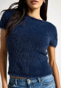 Marineblå fuzzy striktrøje med korte ærmer, der har en struktureret finish og en afslappet pasform, kombineret med denimjeans.