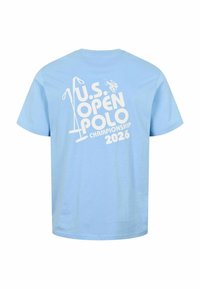 Lyseblå T-shirt med korte ærmer med hvid tekst og grafik med teksten "U.S. Open Polo Championship 2026" og et polo-spillerikon på bagsiden.