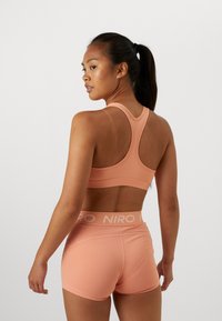 Pink sports bra and shorts set made from smooth, stretchy fabric; features racerback design and logo waistband.