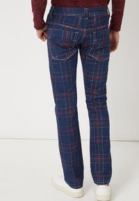Vaqueros de cuadros azules con acentos rojos, que presentan un ajuste Slim, detalles en los bolsillos y costuras en contraste, combinados con zapatillas blancas.
