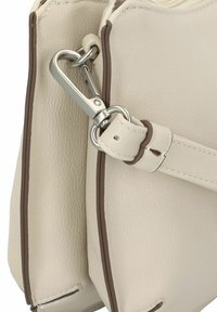 Bolso de mano de cuero crema con acentos en marrón oscuro, que presenta un cierre de metal plateado y una superficie texturizada. Diseño compacto y estructurado.