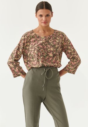 Haut à manches longues à motif floral dans des tons de rose, vert et beige, associé à un pantalon olive à taille ajustable en tissu texturé.