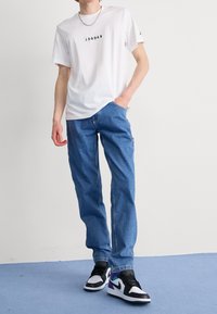 Camiseta blanca con texto negro "JORDAN", jeans azules relajados y zapatillas negras y blancas con acentos morados.