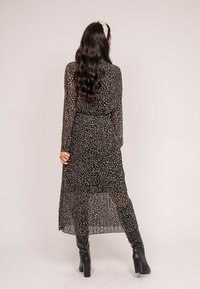 Robe noire à manches longues en tissu transparent, avec un motif à pois blancs et beiges, taille marquée et ourlet longueur cheville.