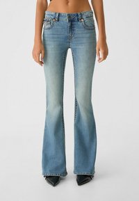 Lysblå flare jeans i slidt denim med middelhøj talje, to forlommer og sølvhardware detaljer.
