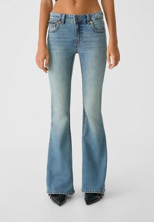 Jean flare bleu clair en denim déchiré, avec une taille mi-haute, deux poches avant et des accents en métal argenté.