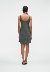 Szürke csillámos szlipruha, alacsony hátkivágással, vékony pántokkal, A-vonalú szabással és puha, texturált anyagból. Fekete magassarkú szandálokkal viselve.