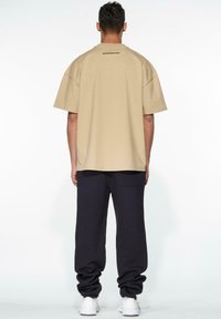 Beige oversized t-paita, jossa on lyhyet hihat ja joka on valmistettu puuvillasta. Takana on pieni musta logo. Yhdistetty tummiin collegehousuihin ja lenkkikenkiin.