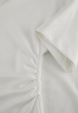 White short-sleeve shirt with ruched detail along the side seam near the underarm area.
