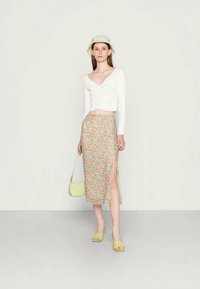 Top cropped de mangas longas branca, saia midi floral com padrões rosa e verde, chapéu balde verde, pequena bolsa verde e sandálias de deslizar verde claro.
