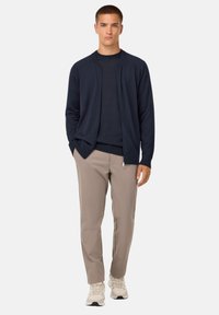 Mornarsko modra jopica z zadrgo, nošena čez usklajen zgornji del, v kombinaciji s svetlimi hlačami in svetlimi športnimi copati. Enostaven dizajn, sproščen kroj.