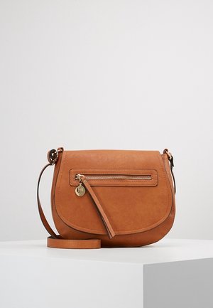 Sac bandoulière en cuir marron avec poche avant zippée, longue bandoulière réglable et tirette de fermeture éclair dorée sur une surface d'exposition blanche.