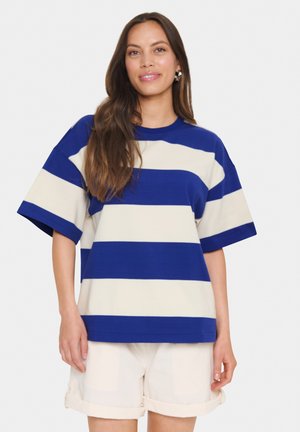 T-shirt a strisce blu e crema con maniche corte e scollatura rotonda, realizzata in tessuto morbido, abbinata a pantaloni corti di colore chiaro.