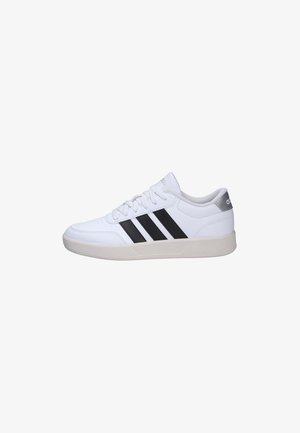 Zapatilla blanca de Adidas con rayas negras, cordones blancos y suela beige, vista de perfil sobre un fondo blanco.