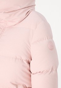 Paminkštas rožinės spalvos švarkas su mažo tarkuoto rašto, aukštu apykakle ir firminiu ženklu viršutinėje rankovėje. Minkšta tekstūra ir quilted dizainas.