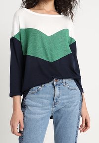 Sweter z zaciemnieniem kolorów w białych, zielonych i granatowych sekcjach; luźny krój, okrągły dekolt i miękka tekstura.