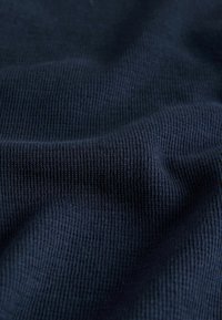 Približni prikaz tamnoplave rebraste tkanine s vidljivom teksturom i mekim naborima koji stvaraju nježne sjene.