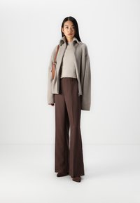 Jasnoszara, prążkowana kurtka zapinana na zamek, beżowy sweter prążkowany, brązowe dopasowane spodnie oraz pasujące brązowe buty. Prosta skórzana torebka w kolorze brązowym.