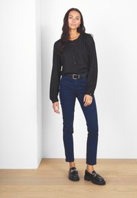 Černá halenka s dlouhým rukávem a knoflíky v kombinaci s námořnickými skinny džíny a černými platformovými mokasíny. Hladká tkanina, přizpůsobený střih a lesklé prvky.