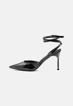 Escarpin à talon aiguille en cuir verni noir, bout pointu, fines lanières à la cheville et petite boucle.