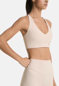 Beige sports bra with a deep V-neck and wide straps, made of smooth material. Paired with high-waisted matching leggings.
