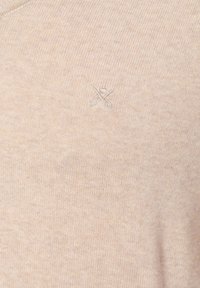 Beżowy sweter z dzianiny o teksturowanym wykończeniu, z małym haftowanym logo nożyczek w jasnoszarym kolorze na lewej piersi.