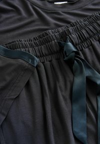 Black garment featuring an elastic waistband with a satin teal ribbon tie, soft texture, and gathered detailing at the waist.
