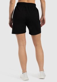 Zwarte katoenen shorts met een elastische tailleband, een zachte textuur en een relaxte pasvorm. Draag ze met witte sportschoenen.