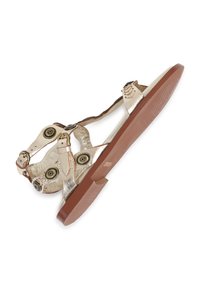 Metallieke gouden sandaal met verstelbare banden, ronde zwarte en gouden accenten, en een bruine gestructureerde zool. Heeft een platte ontwerp.