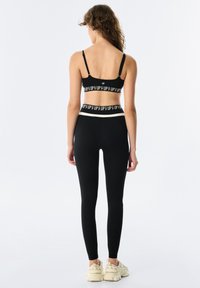 Czarny stanik sportowy z kontrastującym pasem z napisem "UP", w zestawie z czarnymi legginsami o wysokim stanie. Oba elementy charakteryzują się gładką, elastyczną teksturą.