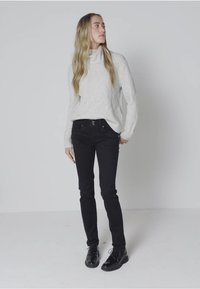 Ljust grått, strukturerat tröja med hög krage, kombinerat med figurnära svarta jeans och svarta snörskor. Enkel, avslappnad outfit.