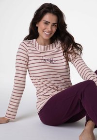 Top a maniche lunghe a righe in crema e bordeaux con scollo a barca; presenta la scritta ricamata "Locatable" sul davanti, abbinato a pantaloni viola scuro.