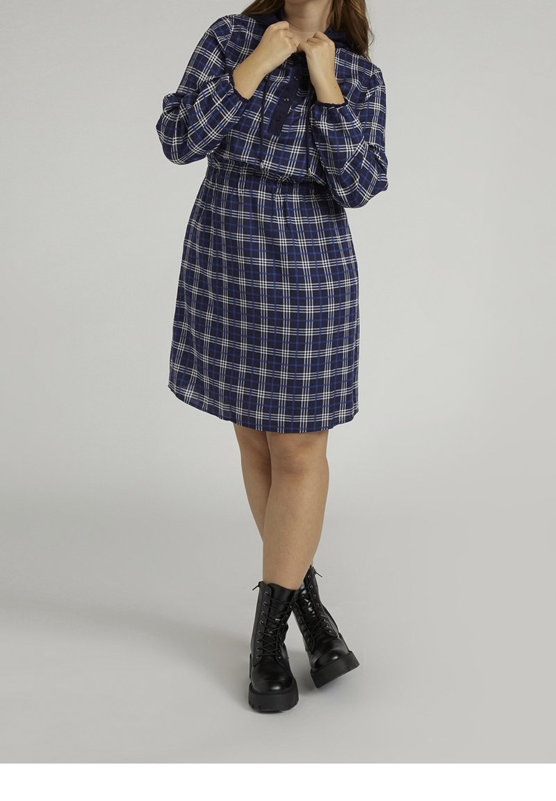 Robe-chemise à carreaux bleu marine avec fermeture à boutons, taille élastiquée, manches longues et ourlet légèrement évasé. Portée avec des bottes de combat noires à lacets.