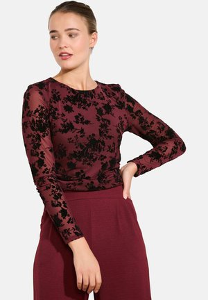 Top a maniche lunghe bordeaux con sovrapposizione in pizzo floreale nero, scollatura rotonda, vita aderente, tessuto morbido e maniche testurizzate.