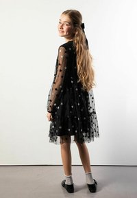 Czarna sukienka z tiulu ozdobiona srebrnymi gwiazdkami, z długimi rękawami, warstwowym krojem i falbanistym dołem. Noszona z skarpetkami i czarnymi butami.