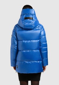 Blå vadderad jacka med hög krage och stor huva. Innehåller quiltade sektioner, sidofickor med blixtlås och en logotypmärke på ryggen.