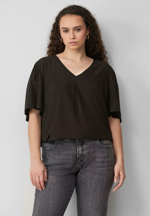 Schwarze V-Ausschnitt-Bluse mit lockeren Ärmeln und einem subtilen Faltendetail in der Mitte. Tragen mit dunkelgrauen Jeans, glatte Textur, entspannte Passform.
