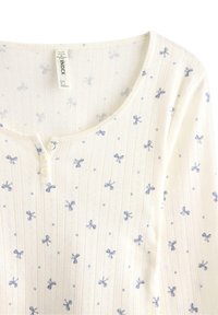 Bomullströja med lång ärm i gräddvitt som har blå blommönster och rosetter, knappslå och ribbad struktur.