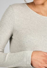 Šviesiai pilkas išilgai raižytas ilgomis rankovėmis viršus su apvaliu iškirpimu ir prigludusia siluetu. Minkšta tekstūra su matomomis siūlėmis ir riešo rankovėmis.