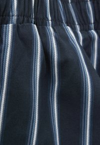 Námořnická modrá látka s bílými a světle modrými vertikálními pruhy, s volante elastickým pasem a texturou typickou pro tkanou bavlnu.