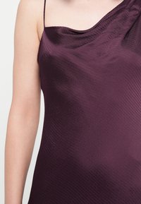 Satijnen, diep paarse jurk met een een-schouderontwerp, een gestructureerde oppervlakte en lichte draping. Verstelbare band aan de linkerkant.