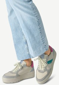 Baskets avec un upper en cuir gris et crème, des accents bleu clair et rose, et une épaisse semelle blanche. Portées avec un jean bleu clair.