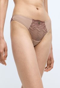 Beige panties featuring sheer textured fabric with wave patterns, accented with dark pink detailing and a small branded logo.