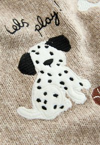 Tissu brodé présentant un Dalmatien noir et blanc ludique sur un fond beige, avec le texte "jouons!" en couture foncée.