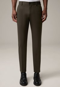 Dunkelgrüne Slim-Fit-Hosen mit glatter Textur, ausgestattet mit einem vorderen Knopfverschluss und einer taillierten Silhouette, kombiniert mit schwarzen Dressschuhen.