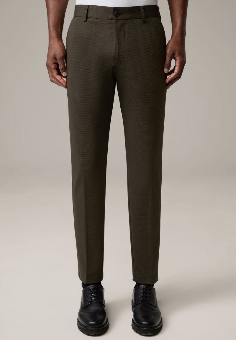 Dunkelgrüne Slim-Fit-Hosen mit glatter Textur, ausgestattet mit einem vorderen Knopfverschluss und einer taillierten Silhouette, kombiniert mit schwarzen Dressschuhen.