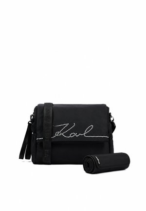 Bolso negro de hombro con decoración de letras tachonadas en la solapa y accesorio negro enrollado al lado sobre fondo blanco.