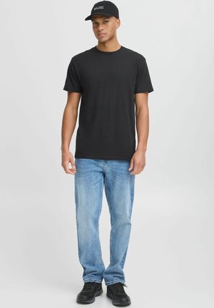 Svart crew-neck t-skjorte, lyseblå denimjeans, svarte sneakers og en svart baseballcap med hvit tekst, som står mot en nøytral bakgrunn.