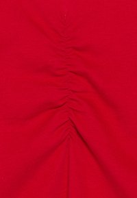 Roter Stoff mit gerafften Details in der Mitte, glatter Textur und einheitlicher, lebendiger Farbe durchgehend.